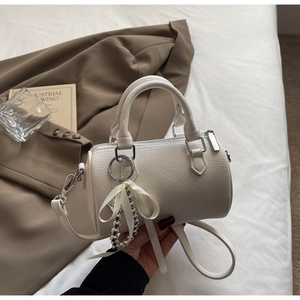 Gros plan sur un mini sac Boston blanc avec nœud en ruban et pendentif métallique