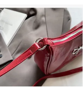 Detailed close-up of dark red glossy shoulder bag with silver bow charm and zipper