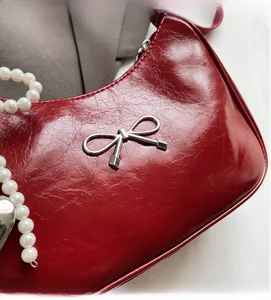 Detail of red faux leather handbag with silver metallic bow and pearl chain accent