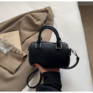 Détail du sac polochon noir en cuir grainé avec finitions argentées sur un lit blanc