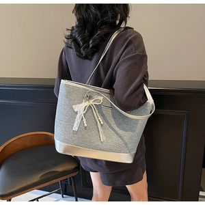 Gros plan d'un sac cabas en tissu gris avec garniture argentée et nœud en dentelle blanche