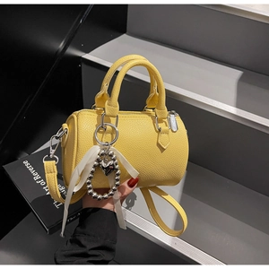 Détail macro du sac Boston en cuir jaune avec ruban et breloque en forme de cœur