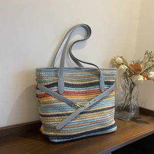 Chic multi-color striped woven straw tote bag with blue leather handles on wooden table