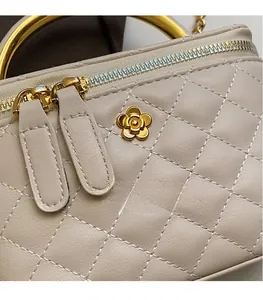 Detail of beige quilted bucket bag with gold floral hardware and dual metal zippers