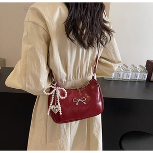 Detail of burgundy half-moon shoulder bag with silver bow and pearl heart charm