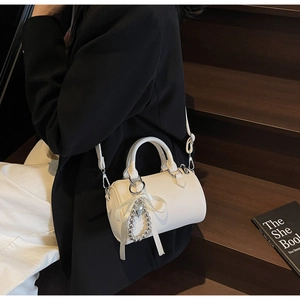 Détail du sac Boston en cuir litchi blanc avec breloque perle sur fond bois sombre
