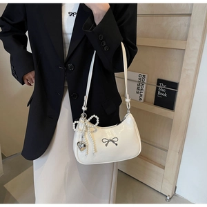 Detail of white half-moon underarm bag featuring a metallic bow and pearl heart charms