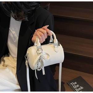 Détail macro du cuir grainé blanc d'un sac Boston avec breloque perle et ruban