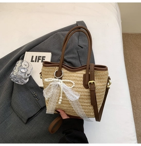 Detail of straw tote bag with white lace bow, pearl charm, and brown leather handle