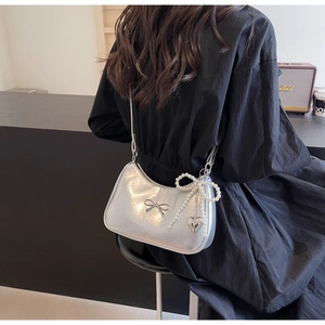 Silver shoulder bag with bow, pearl chain and heart charm detail on a model