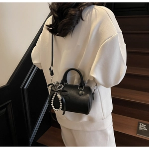 Sac oreiller noir chic avec nœud et breloque cœur porté à l'épaule pour un look décontracté