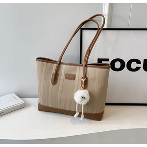 Detail of beige tote bag with wavy texture, brown leather trim and fuzzy charm