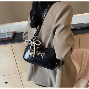 Detail of black patent leather underarm bag with silver bow and pearl charm