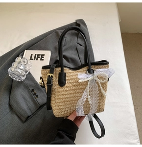Detail of straw woven bucket bag with black leather handle and pearl lace bow charm