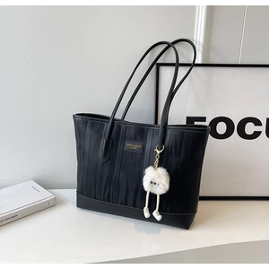 Detail of black wave-patterned tote bag with white plush charm on a minimalist desk