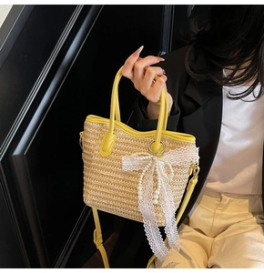 Detail of yellow leather handle and lace bow with pearls on straw bucket tote bag