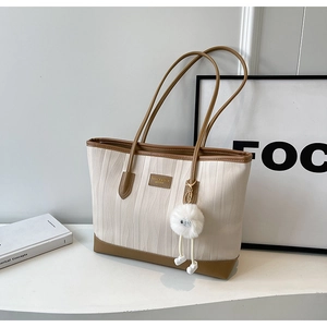 Detailed close-up of a cream tote bag with contrast brown trim and plush ball charm