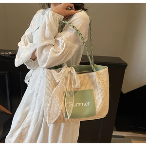 Detail of straw tote bag featuring green straps, lace bow, and summer leather patch