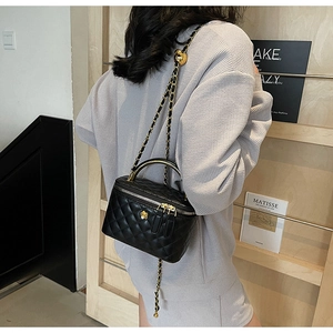 Detail of black quilted vanity bag with gold chain strap and floral metal zipper charm