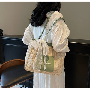 Detail of straw tote bag featuring green leather trim, summer print and large lace bow