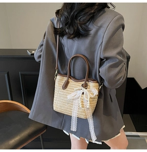 Straw tote bag detail with brown leather trim, white lace bow, and pearl decoration