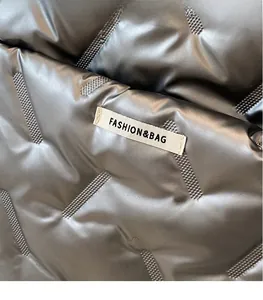 Macro detail of silver metallic puffer fabric with Fashion & Bag woven label and quilting