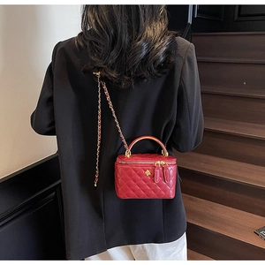 Detail of red quilted mini box bag with gold metal handle and chain strap on model