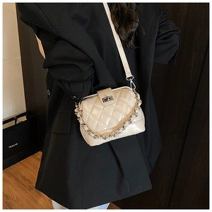 Detail of cream quilted crossbody bag with silver chain worn over a black blazer