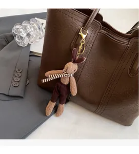 Close-up of a brown knitted bunny charm with striped scarf on a leather tote bag