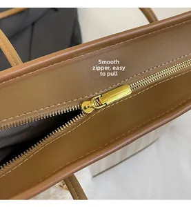 Detailed close-up of smooth gold metal zipper and precision stitching on brown tote bag