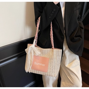 Close-up of straw tote bag with pink braided handle, lace bow, and Summer patch
