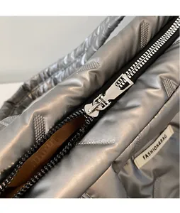 Detailed close-up of quilted metallic silver fabric and smooth zipper puller on tote bag