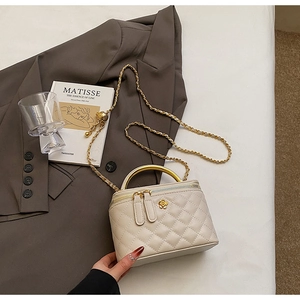 Close-up of beige quilted bag featuring golden camellia clasp and sleek metal handle