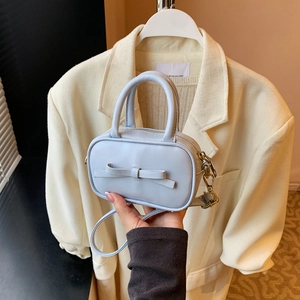 Close-up of light blue mini bag with leather bow and gold hardware in hand-held pose