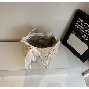 Top view of woven straw tote bag with green Summer text and lace bow on marble surface