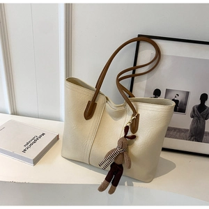 Detail of creamy white tote bag with brown straps and cute rabbit doll keychain charm