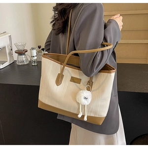Detail of beige textured tote bag with contrast brown straps and plush ball charm