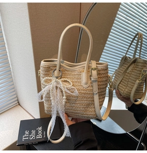 Straw bucket bag detail with lace bow, pearl charm and leather handles in soft lighting