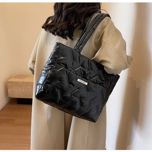 Close-up of black quilted tote bag with white fashion label on a model shoulder