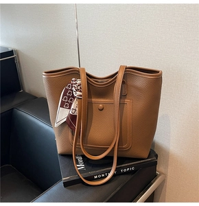 Brown lychee texture leather tote bag with silk scarf detail on a black leather sofa