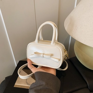 Detailed view of cream mini bow bag size comparison held by hand with golden hardware