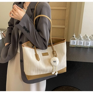 Detail of cream contrast tote bag with brown leather trim and plush charm on female model