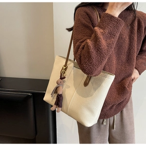 Detail of a beige tote bag with litchi texture and a brown plush rabbit charm