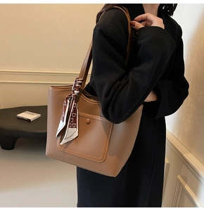 Detail of tan leather tote bag with silk scarf accessory and button pocket