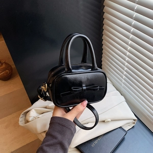 Detail of a mini black crossbody bag with bow accent and gold hardware on book