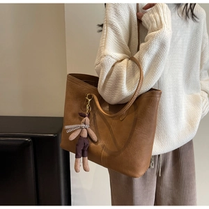 Detail of a large brown vintage tote bag with contrast stitching and a rabbit plush charm