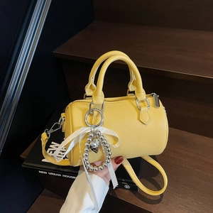Sac Boston jaune vif en cuir lychee avec pendentif noeud sur marches en bois sombres