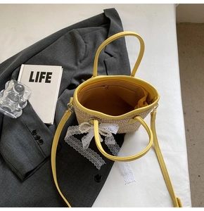 Detail of straw bucket bag with yellow leather trim, lace bow, and pearl charm