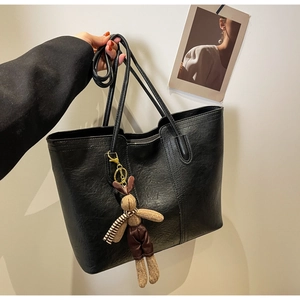 Detail of black pebbled leather tote bag featuring a cute plush bunny charm and dual handles