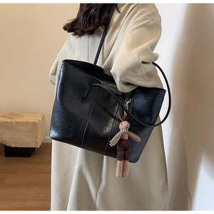 Detail of black pebbled leather tote bag with stylish plush bunny charm and shoulder straps